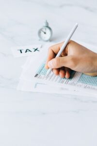 Main remplissant des formulaires fiscaux avec un stylo, symbolisant l'échéance financière et l'urgence du temps.